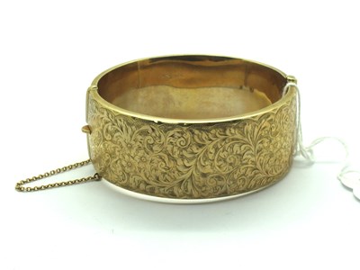 Lot 134 - A 9ct Gold Wide Hinged Bangle, scroll engraved...
